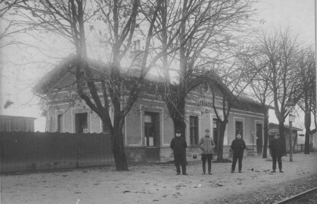 Historische Schwarz-Weiß-Aufnahme des Bahnhofs Erlach mit vier Personen vor dem Gebäude